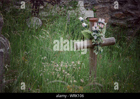 Wooden cross with plastic flowers among the grass. Stock Photo