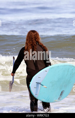 A surfer prepares to enter the water at Newcomb Hollow Beach, Wellfleet, Massachusetts on Cape Cod, USA. Stock Photo