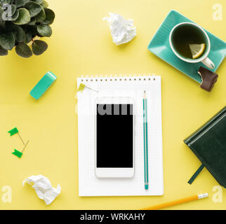 Stylized clean yellow office working desk with smartphone, notepad, pencil and tea, workspace design, mock up, top view, flat lay, copy space, closeup Stock Photo