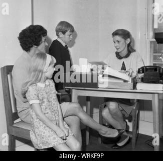 1970s, historical, a mother with her two young children sitting with a female  secretary or receptionist in an office, England, UK. Stock Photo