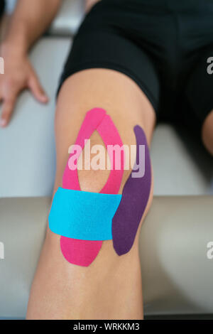 Top view of a patient's knee with three medical straps, purple, light blue and pink. Concept of muscle health and relaxation. Vertical image Stock Photo