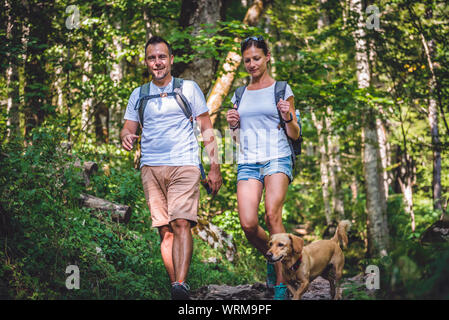 Couple with a small yellow dog hiking in forest Stock Photo