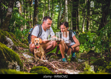 Hiking couple with small yellow dog checking map in forest Stock Photo