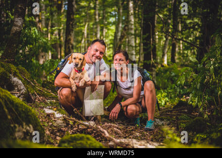 Hiking couple with small yellow dog posing in forest Stock Photo