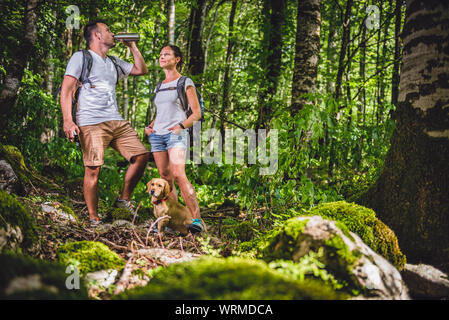 Hiking couple with small yellow dog resting and drinking water Stock Photo