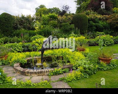 Chenies Manor sunken garden oval ornamental pond, terraced plant borders and sculpure of diver by Alan Biggs framed by lush green foliage and hedges, Stock Photo