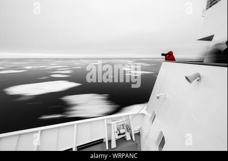 Tourist in the Arctic taking a photo while standing on top of a ship with icebergs passing by, Svalbard, Norway Stock Photo
