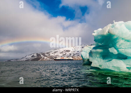 Cruise ship under a rainbow cruising past an iceberg in Hornsund Svalbard Norway within the arctic circle. Stock Photo