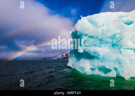 Cruise ship under a rainbow cruising past an iceberg in Hornsund Svalbard Norway within the arctic circle. Stock Photo