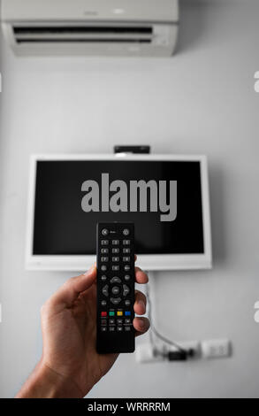 The man with the remote control in hand want switch on the TV and presses the button on the remote control. Remote control in hand closeup. Stock Photo