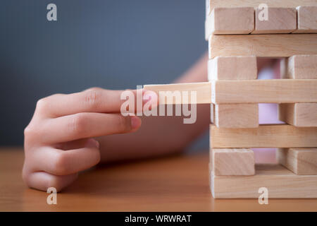 Hand of a girl placing and pulling wooden block on the tower. Alternative risk concept, plan and strategy in business and education. Stock Photo