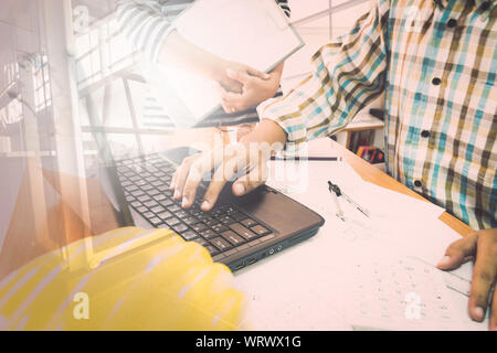 Double exposure of architect with partner working with laptop on construction plan in office Stock Photo