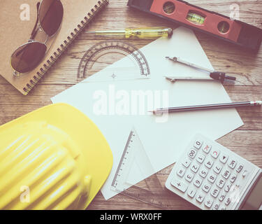 Paperwork with writing materials, construction helmet, sunglasses, notepad, calculator and construction tools for architecture on wooden table Stock Photo