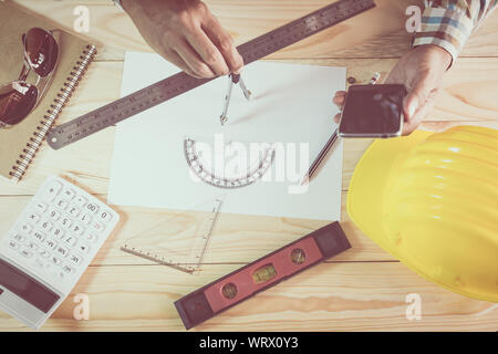 Hands of architect drawing construction plan and holding smart phone on wooden desk Stock Photo