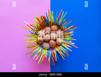 Chicken eggs in a basket on pink and blue paper background, Easter eggs concept. Stock Photo