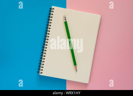 Open notebook with green pencil isolated on pink and blue paper background, Education concept. Stock Photo