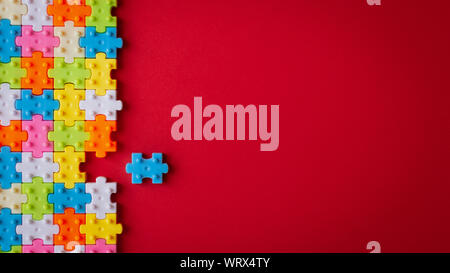 Colors plastic jigsaw puzzle on red paper background, Missing one jigsaw puzzle to complete with copy space, Business strategy teamwork and problem so Stock Photo
