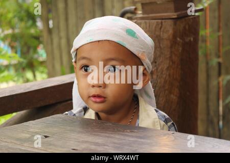Portrait Of Cute Boy Wearing Bandana While Standing At Wooden Table