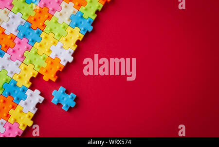 Colors plastic jigsaw puzzle on red paper background, Missing one jigsaw puzzle to complete with copy space, Business strategy teamwork and problem so Stock Photo