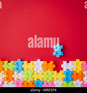 Colors plastic jigsaw puzzle on red paper background, Missing one jigsaw puzzle to complete with copy space, Business strategy teamwork and problem so Stock Photo
