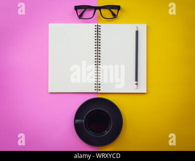 Blank white notepad with black coffee cup, pencil and glasses on two tone pink and yellow background. Business inspiration concepts. Stock Photo