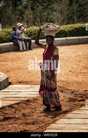 Indian woman in colorful saree carrying rocks in a basket on her head at Shore Temple, Mahabalipuram, India Stock Photo