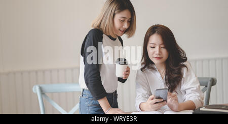 Two young freelancers chatting and looking at smartphone together during the free time Stock Photo