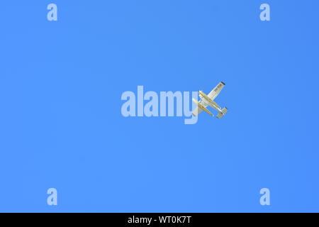 Distant small white airplane with floats under fuselage in bright sunlight against blue sky. Stock Photo