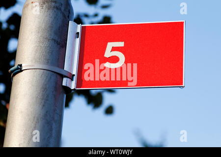 red sign with white text outdoors with the number five, a small drop of water at the bottom of the sign Stock Photo