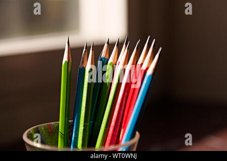 colored pencils in a drinking glass on the desk with afternoon sun coming in through the office window Stock Photo