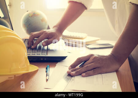 Hands of architect working on laptop with construction plan under shinning light in office Stock Photo