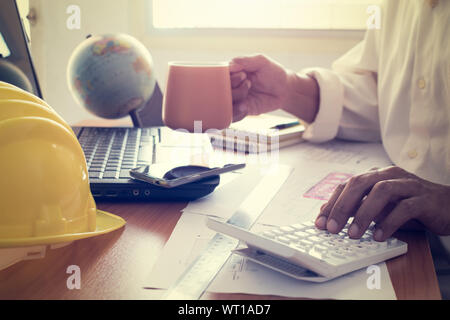 Hands of architect on calculator and holding coffee cup on office desk Stock Photo