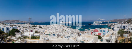Panoramic view of Mykonos town with white houses and sailing cruise ships in blue sea on sunny day in Greece Stock Photo