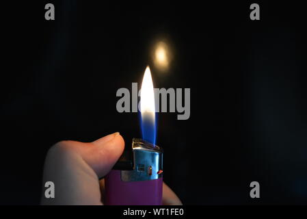 The fire and the included pink plastic lighter lie in a female hand on a black glossy surface. Stock Photo