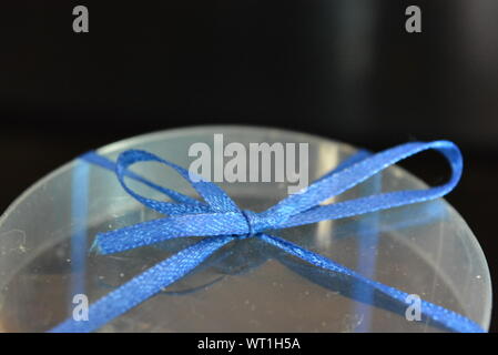 Blue teddy bear made of natural wax is made in the shape of a candle and packed in a plastic box with blue bow on black glossy background. Stock Photo