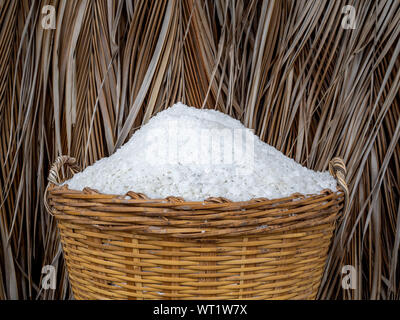 White sea salt in yellow basket on dried tropical palm leaves background. Salt farming, salt process production concept. Stock Photo