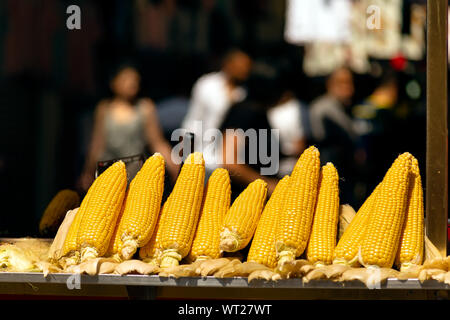 Raw corn on cobs and fire roasted corns displayed together on a street vendor cart bench. Stock Photo