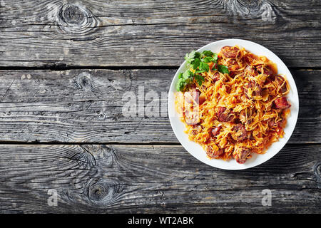 delicious Cabbage stew with sliced sausages served on a white plate on a wooden table, view from above,  flatlay, empty space Stock Photo