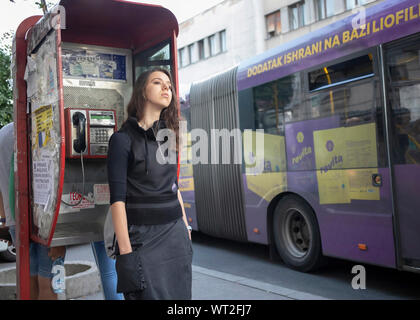 Belgrade, Serbia, September 10th 2019: Young woman standing on the sidewalk leaning against a pay phone at Glavna Street in Zemun Stock Photo