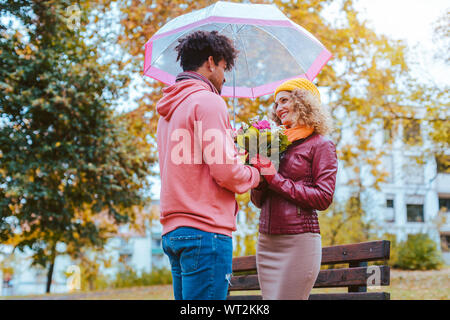 Black man giving flowers to his Caucasian girlfriend in fall Stock Photo