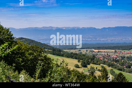 City landscape in the mountains, hills, fields, forests, green meadows, lakes in the distance and blue sky with clouds.Town Bons-en-Chablais in France. Stock Photo