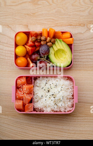 Creative layout with healthy lunch dishes variety in bento boxes on wooden table. Sandwich, slad with grains and pomegranate seeds, salmon with rice a Stock Photo