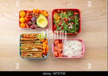 Creative layout with healthy lunch dishes variety in bento boxes on wooden table. Sandwich, slad with grains and pomegranate seeds, salmon with rice a Stock Photo