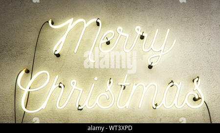 Neon sign that says the word Merry Christmas in bright white on a grunge concrete wall background, Christmas decoration sign Stock Photo