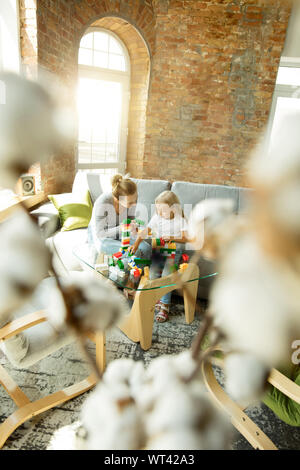 Female caucasian teacher and little girl, or mom and daughter. Homeschooling. Sitting on the sofa with plastic constructor, learning, talking and having fun. Education, school, studying concept. Stock Photo