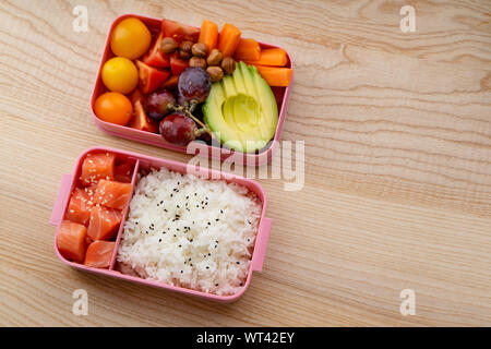 Creative layout with healthy lunch dishes variety in bento boxes on wooden table. Sandwich, slad with grains and pomegranate seeds, salmon with rice a Stock Photo