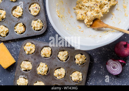 Cheddar cheese and herbs mini muffin dough uncooked being placed in muffin baking trays - overhead view Stock Photo