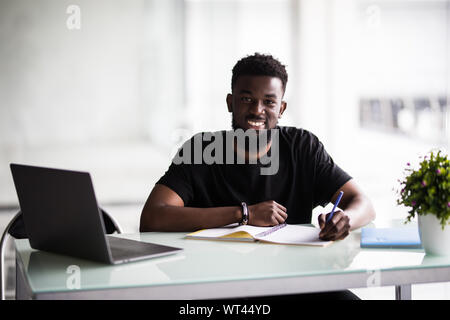 Young man working on his laptop in office. Young african executive sitting at his desk surfing internet on laptop computer. Stock Photo