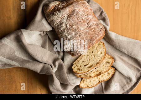 Whole sourdough bread loaf on kitchen cloth on rustic wooden table - Overhead photograph Stock Photo