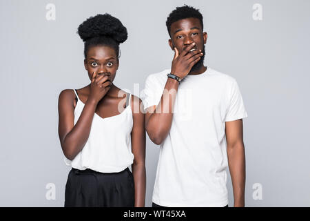 African couple in denim shirts covering their mouths while looking at the camera over grey background Stock Photo